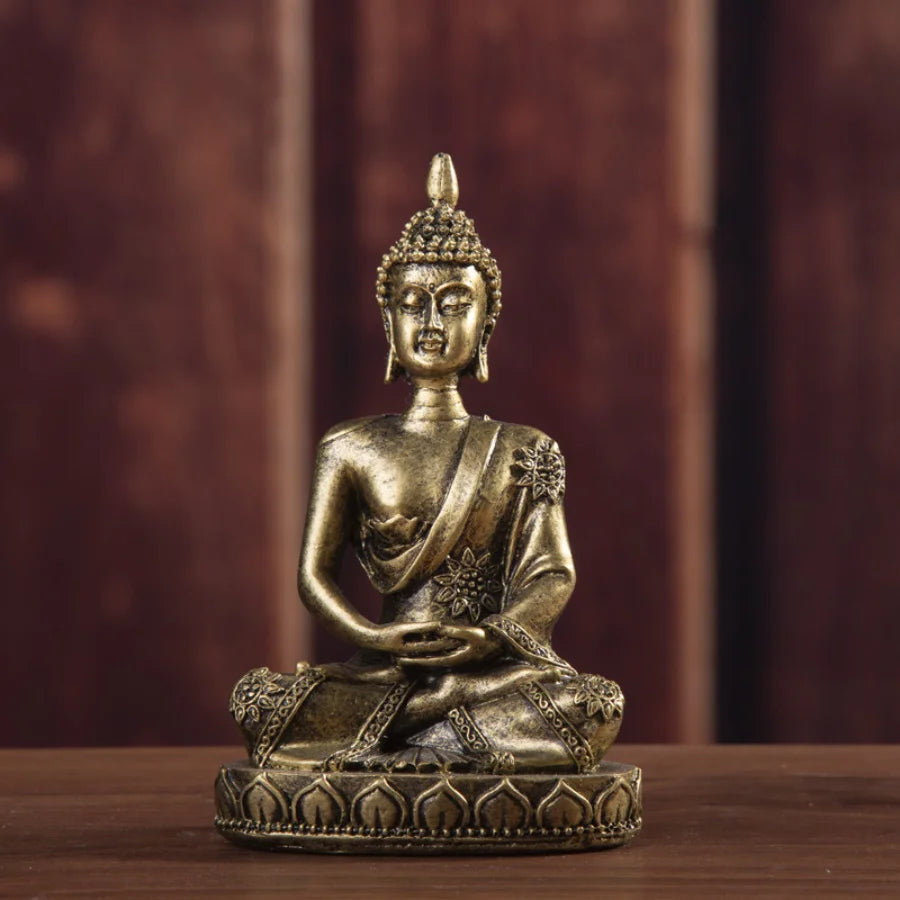 A handcrafted resin Buddha statue in gold tone seated in meditation on a wooden surface.