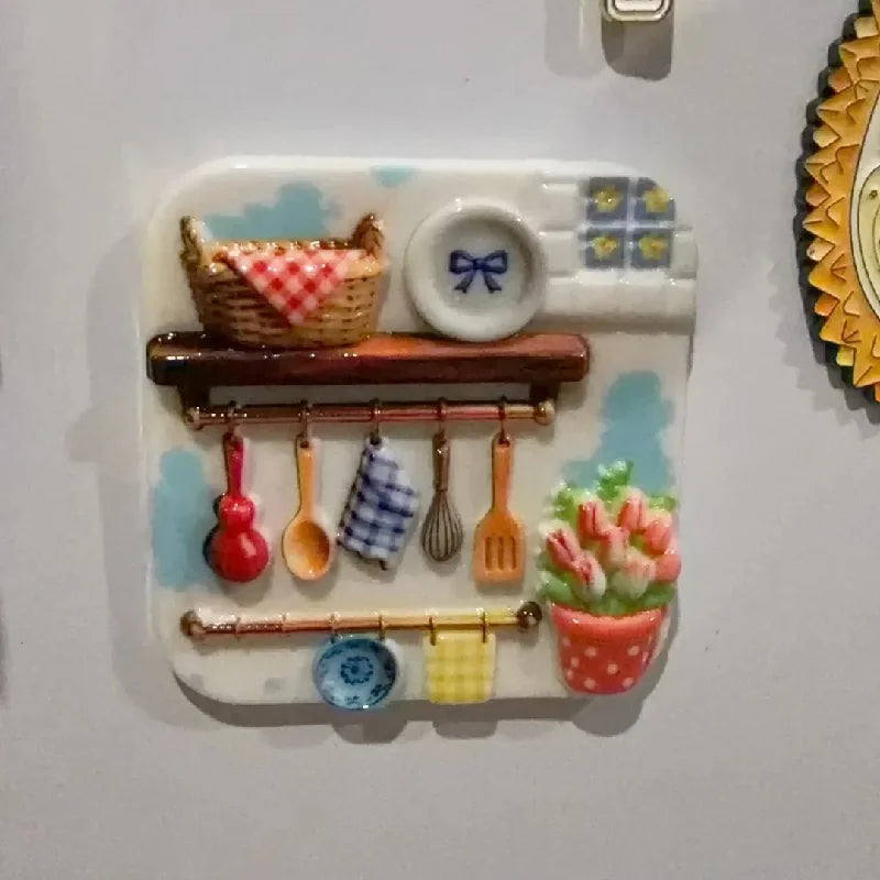 A white resin fridge magnet featuring a woven basket, a small bowl with a bow, and various kitchen utensils hanging on a wood