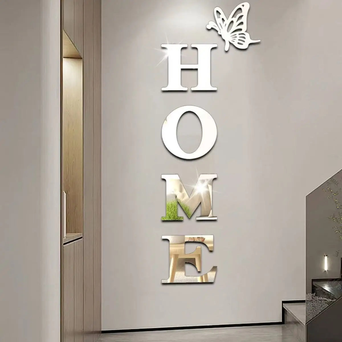 A wall decor set featuring the letters H O M E formed by butterfly-shaped acrylic mirror stickers on a white wall.