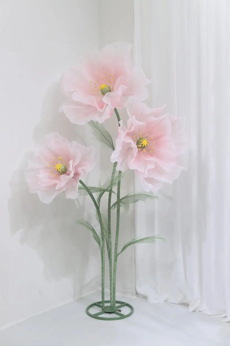 A large artificial silk pink poppy flower displayed on a green stand against a white background.