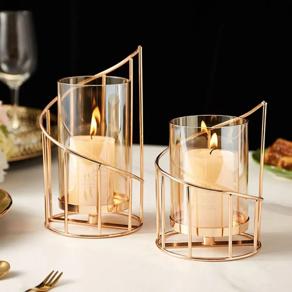 Elegant gold metal candle holders with glass cylinders and flickering candles on a white surface.