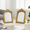 A pair of ornate gold-framed vanity mirrors with arched carvings resting on a white table.