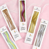 A set of six curved decorative birthday candles in various colors and metallic shades displayed on white packaging.