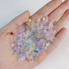 Una mano sostiene una pila de 50 mini aderezos para uñas de tortugas de colores, en tonos rosa, azul y amarillo.
