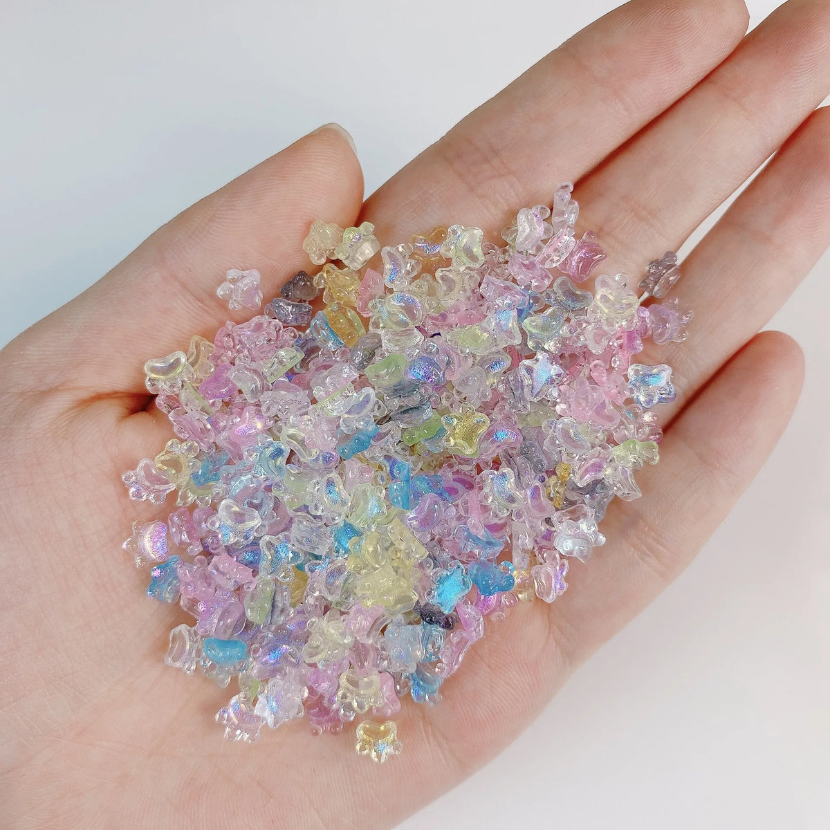 Una mano sostiene una pila de 50 mini aderezos para uñas de tortugas de colores, en tonos rosa, azul y amarillo.