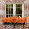 A window box filled with bright orange and white artificial fall eucalyptus and flower stems against a brick wall.