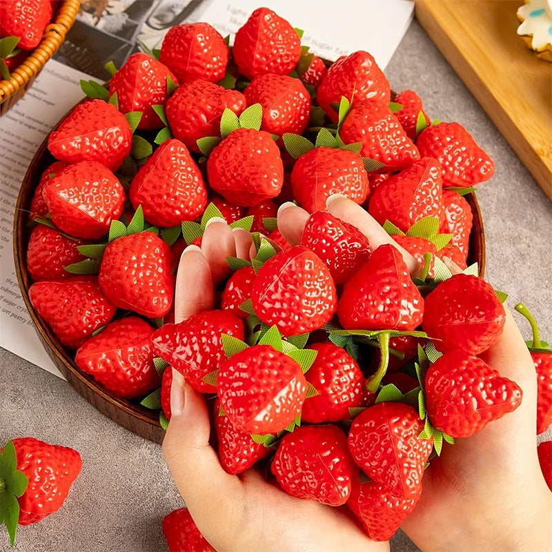 A hand holds a bowl full of bright red artificial strawberries for home decor or party styling.