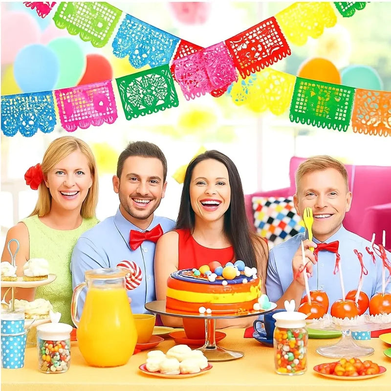 A colorful fiesta papel picado bunting banner decorated with bright paper flags and fruit on a table.