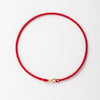 A handmade red string bracelet with a gold plated clasp laid flat on a white background.