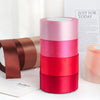 Un ensemble de rubans décoratifs en satin dans des tons de rose, rose et rouge sont présentés sur une surface blanche.