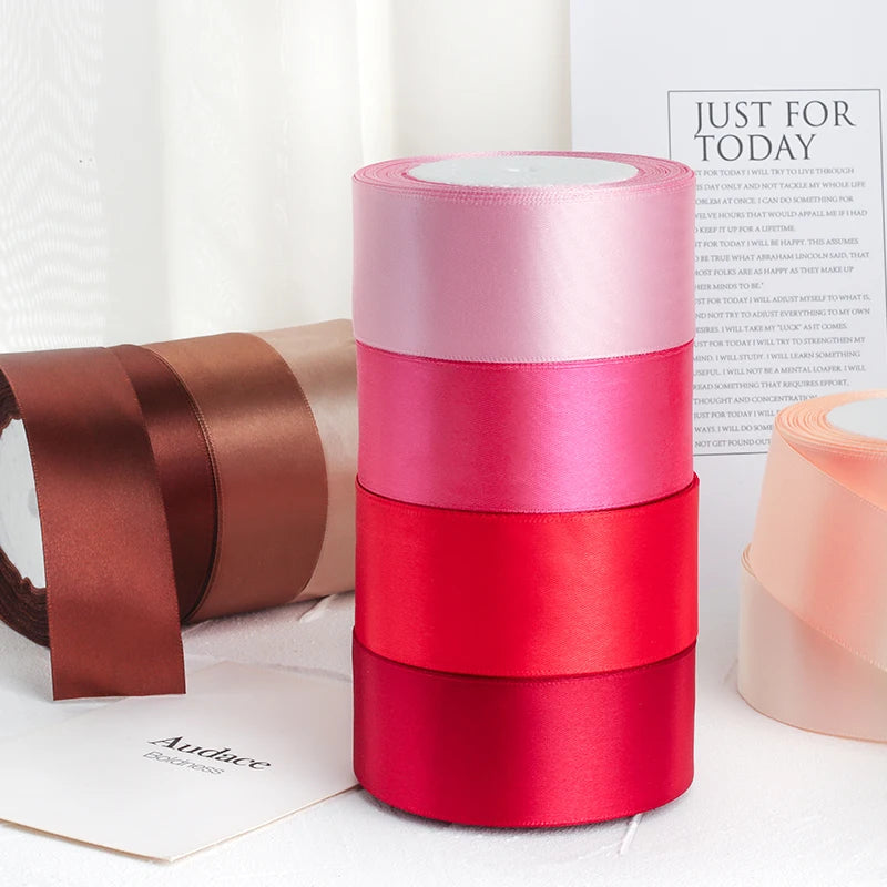 Un ensemble de rubans décoratifs en satin dans des tons de rose, rose et rouge sont présentés sur une surface blanche.