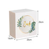 A rectangular white acrylic gift box with a circular gold wreath design and green foliage.