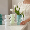 A woman holds a white dress and a glass flower vase with white tulips on a white countertop.