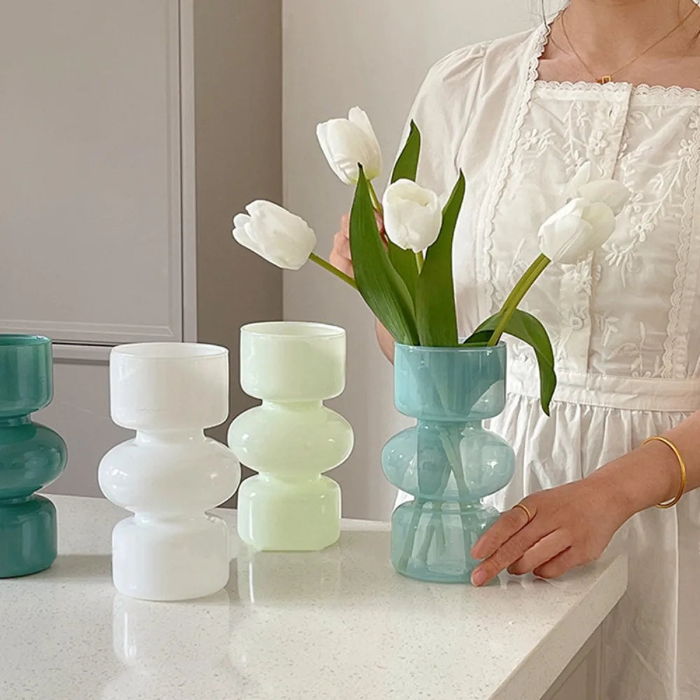 A woman holds a white dress and a glass flower vase with white tulips on a white countertop.