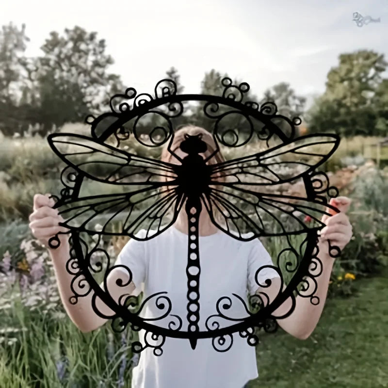 A person holds up an elegant black dragonfly metal wall art piece outdoors.