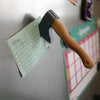 A wooden axe is attached to a light green card, used as a fridge magnet for kitchen decor.