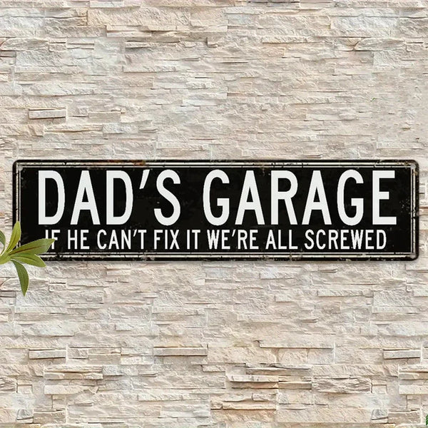 A black tin sign mounted on a light stone wall with the text Dad's Garage If he can't fix it we're all screwed