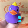 A purple rubber duck bath toy with an orange beak and a yellow crown is held in a hand.