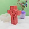 A pink silicone mold shaped like a religious Jesus cross, displayed next to white candles and a purple vase with flowers.