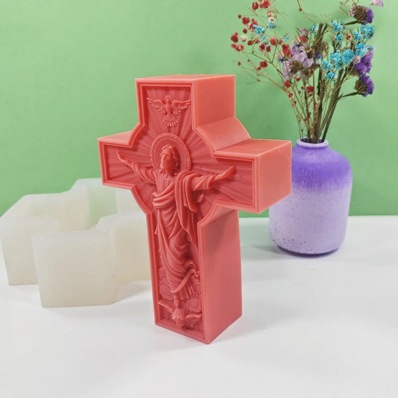 A pink silicone mold shaped like a religious Jesus cross, displayed next to white candles and a purple vase with flowers.