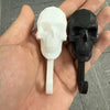 A set of two decorative skull wall hooks, one white and one black, held in a person's hand.