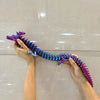 A hand holds a long, purple and blue articulated dragon figurine with intricate scales.