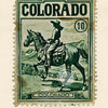 A vintage postage stamp featuring a depiction of a cowboy riding a horse in a western landscape.
