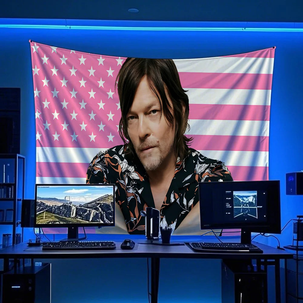 A man with long hair is positioned in front of a large American flag banner decorated with pink and white stripes and stars.