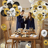 A table decorated with gold and white graduation balloons featuring caps and stars, surrounded by people.