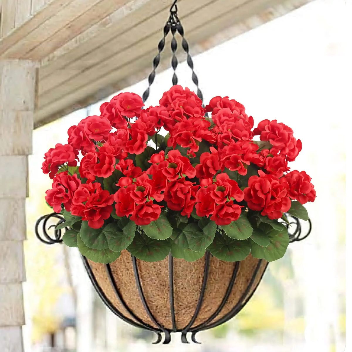 A hanging basket filled with bright red artificial geranium flowers on a rustic hanger.