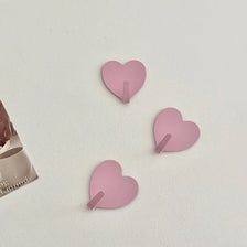 Three pink heart-shaped adhesive hooks are displayed on a white surface.