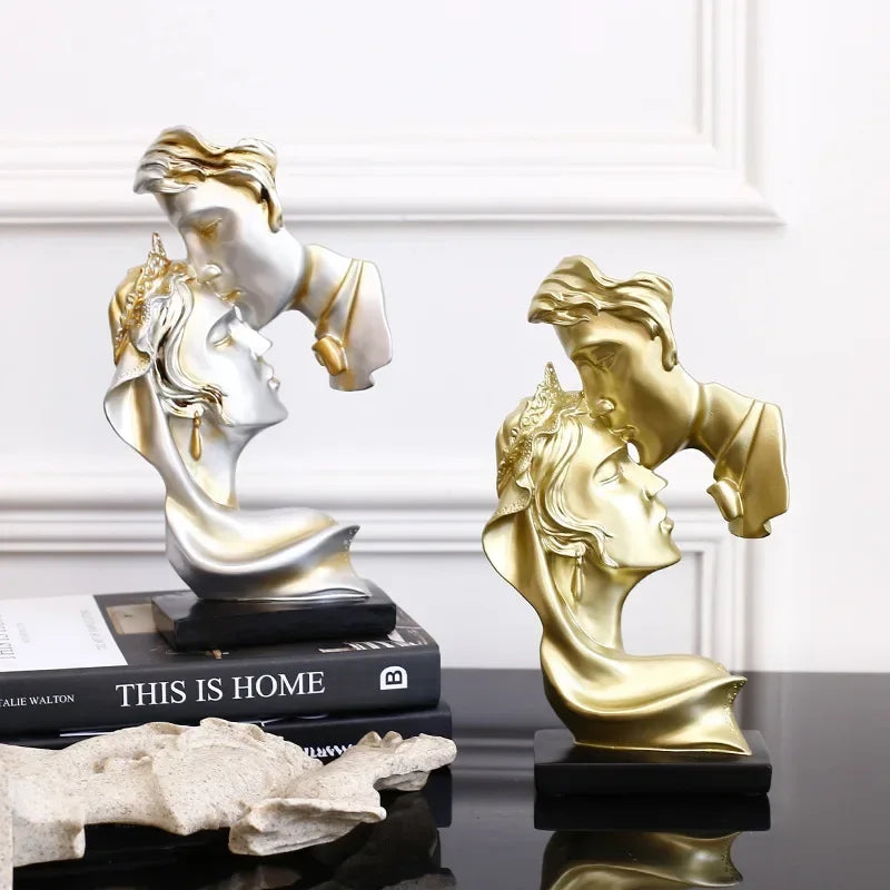 Une paire de statues miniatures en résine, une argentée et une dorée, exposées sur une surface sombre.