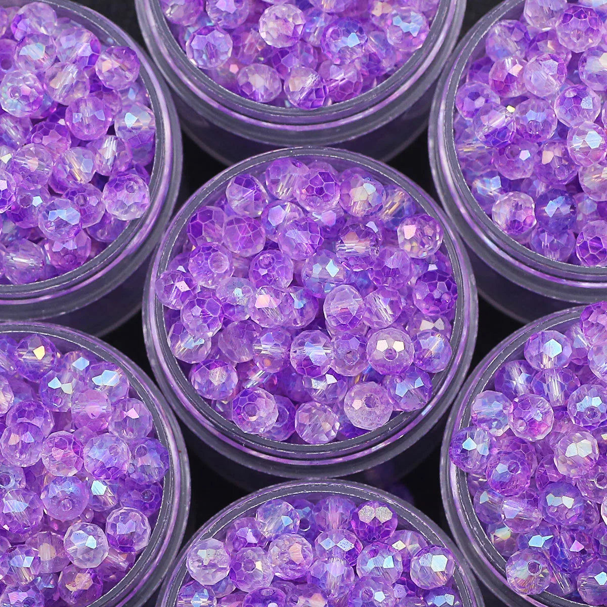 A close-up view of purple AB crystal glass beads in small jars for jewelry making.
