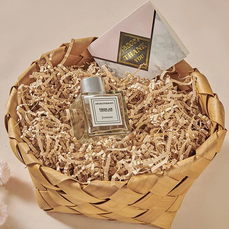 Ein Glasflakon Aromatherapie-Jasminparfüm in zerknüllten Papiertäschchen in einem geflochtenen Korb.