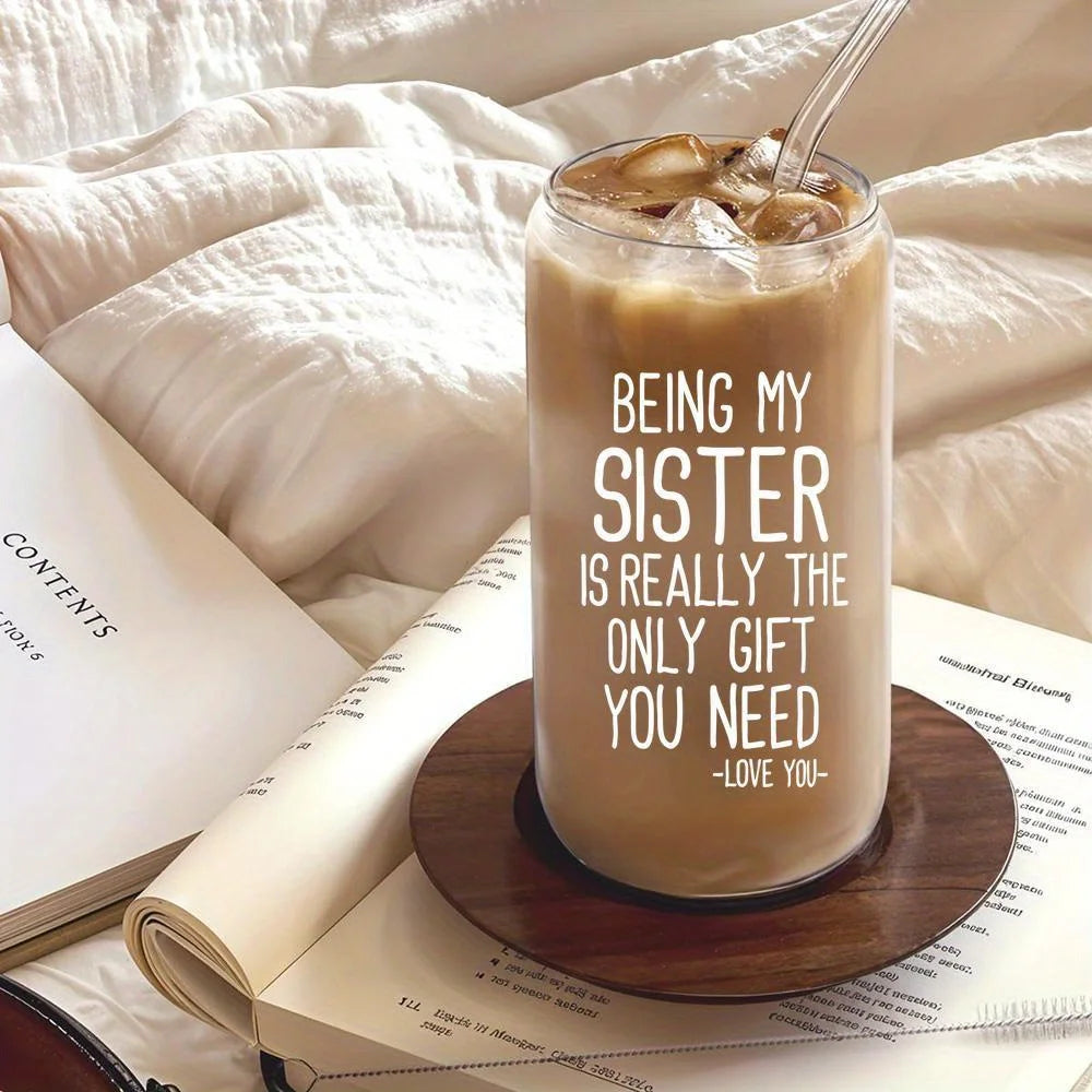 A clear glass tumbler filled with iced coffee sits on a book surrounded by soft white fabric.