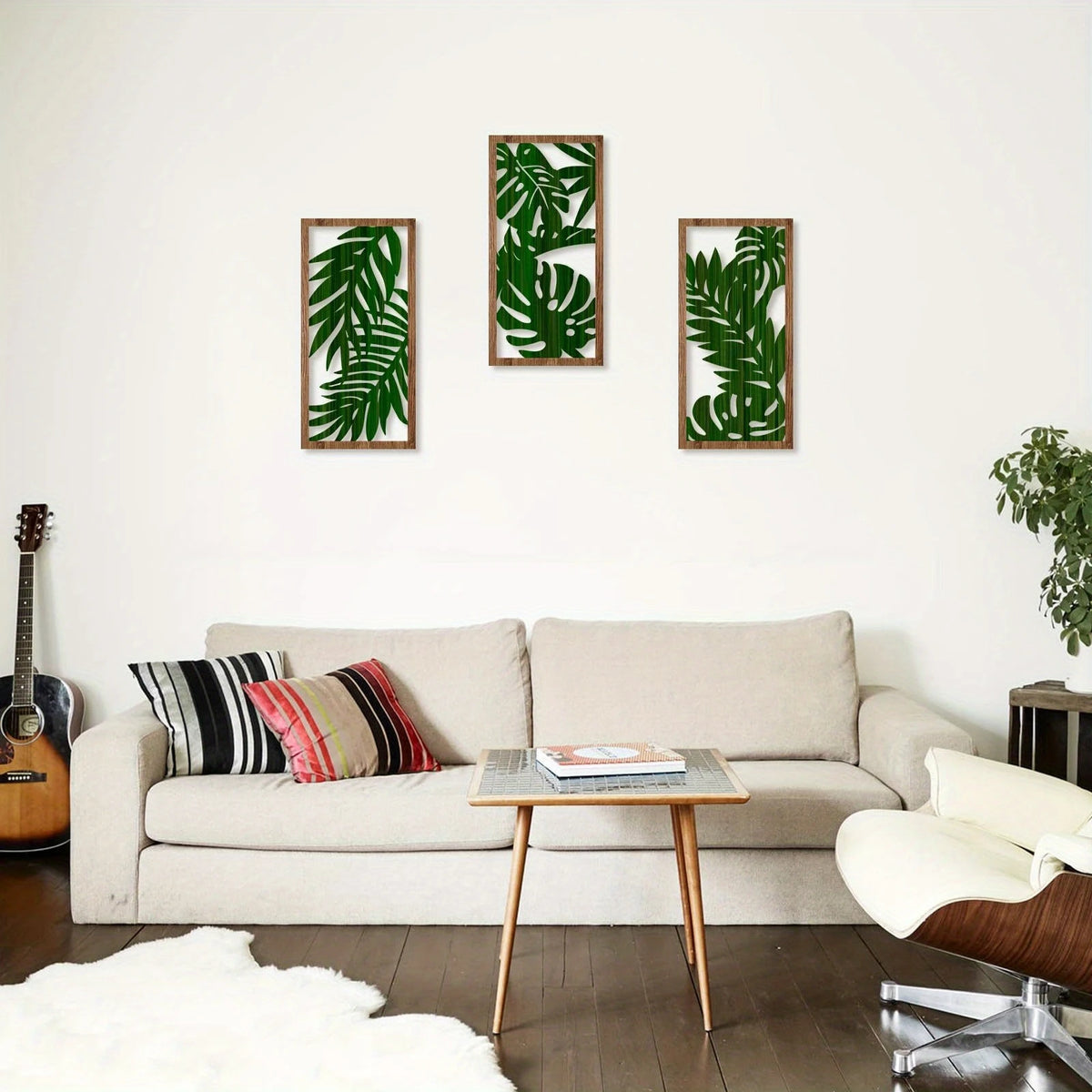A living room wall decorated with three framed green tropical leaf prints above a light sofa.