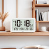 A white digital wall clock displaying the time 10:18 AM, date, temperature, and humidity on a wooden shelf.