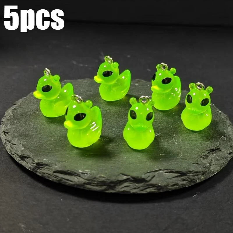 Five glow-in-the-dark green cartoon alien kitty duck resin charms displayed on a dark surface.