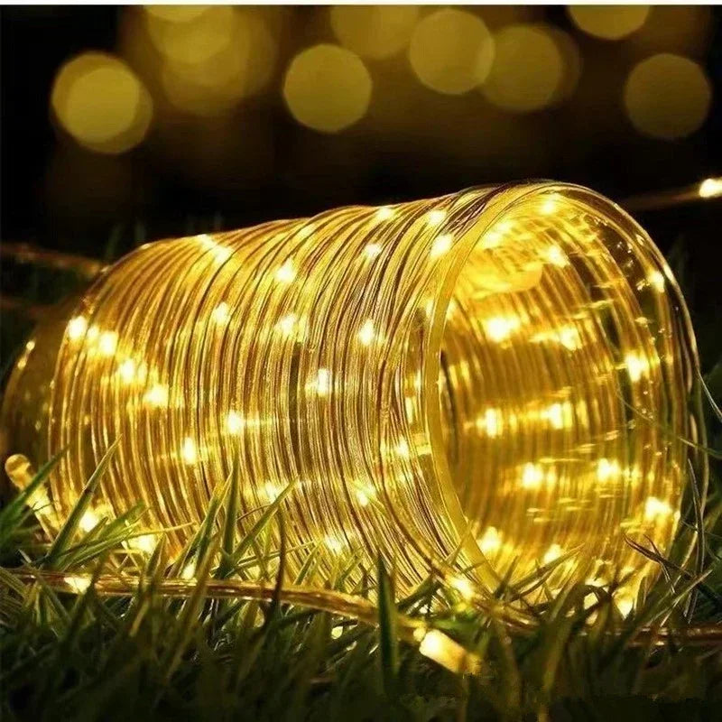A coiled yellow LED rope light illuminates green grass at night.