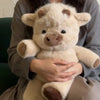 Une personne tient une peluche de veau écossais moelleuse de couleur claire.