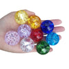 A hand holds several colorful, translucent crystal ice crack balls in various shades of yellow, purple, blue, and green.