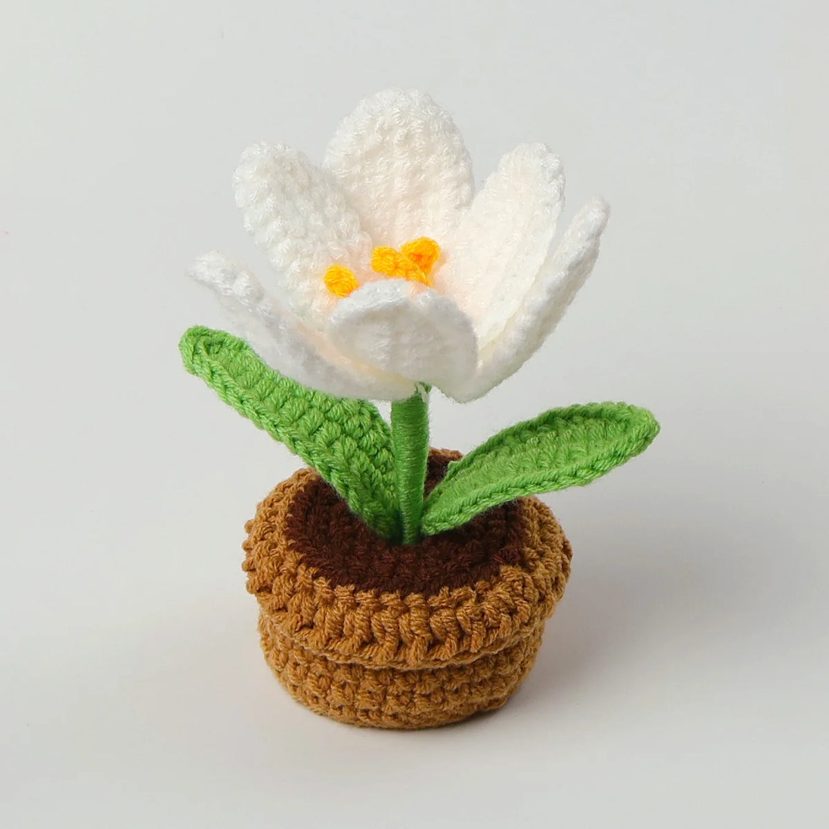 Handcrafted white crochet tulip flower with yellow center growing in a brown crocheted pot and green leaves