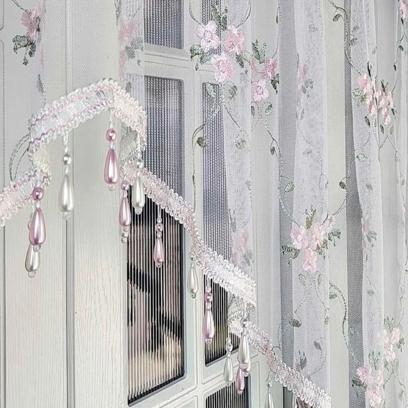 Elegantes Dreieckstüll-Vorhang mit rosa Blumenstickerei und Perlentropfen auf einem weißen Holzfensterrahmen