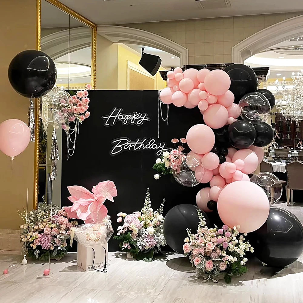 A floral and balloon display featuring pink, black, and white balloons and flowers for a celebration.