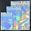 Three clear holographic rainbow resealable bags stacked on a dark surface.