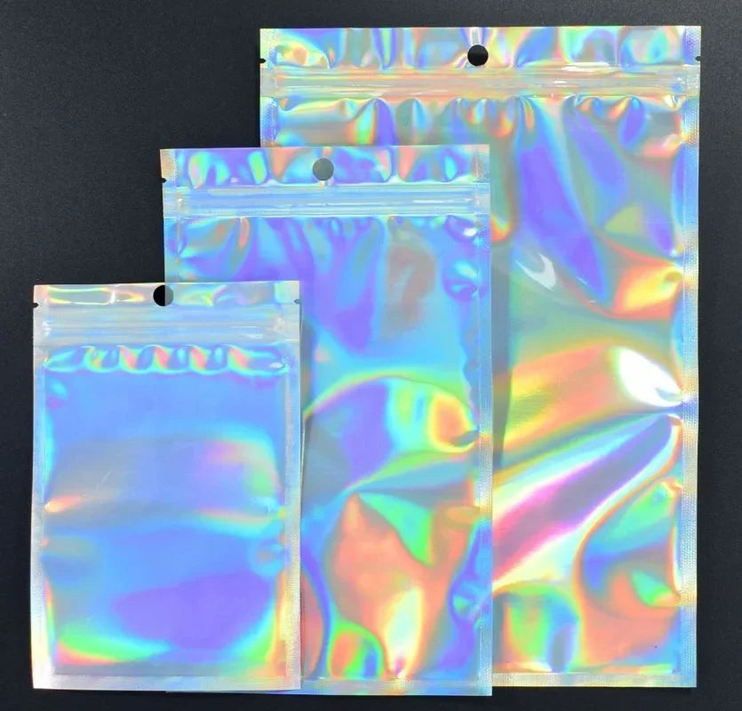 Three clear holographic rainbow resealable bags stacked on a dark surface.
