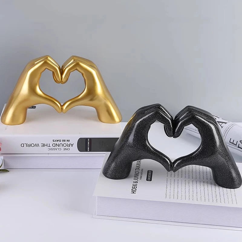 Gold and black resin heart-shaped hand sculptures displayed on a stack of books.
