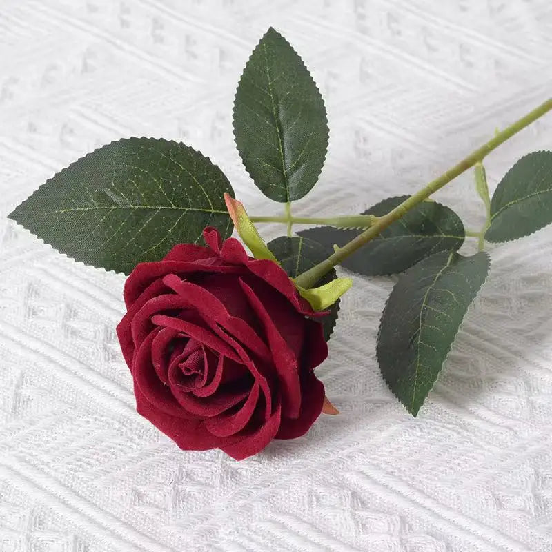 A deep red velvet artificial rose with green leaves on a stem.