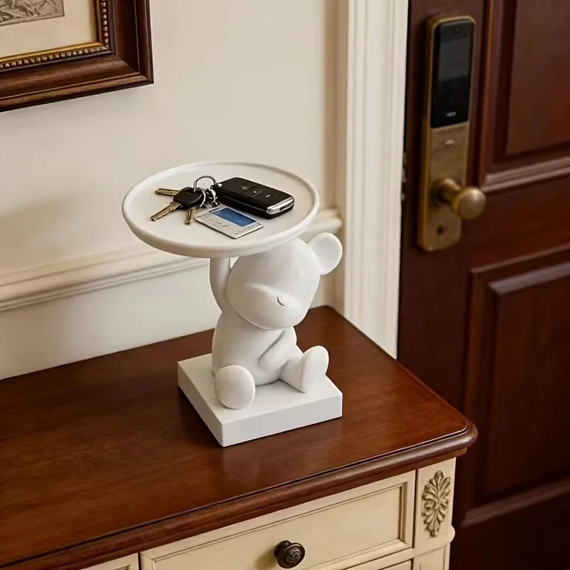 A white bear figurine holds a tray with keys and accessories on a wooden cabinet top.