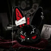 A black bunny plush keychain with red accents and lightning bolt markings resting on a dark red fabric.